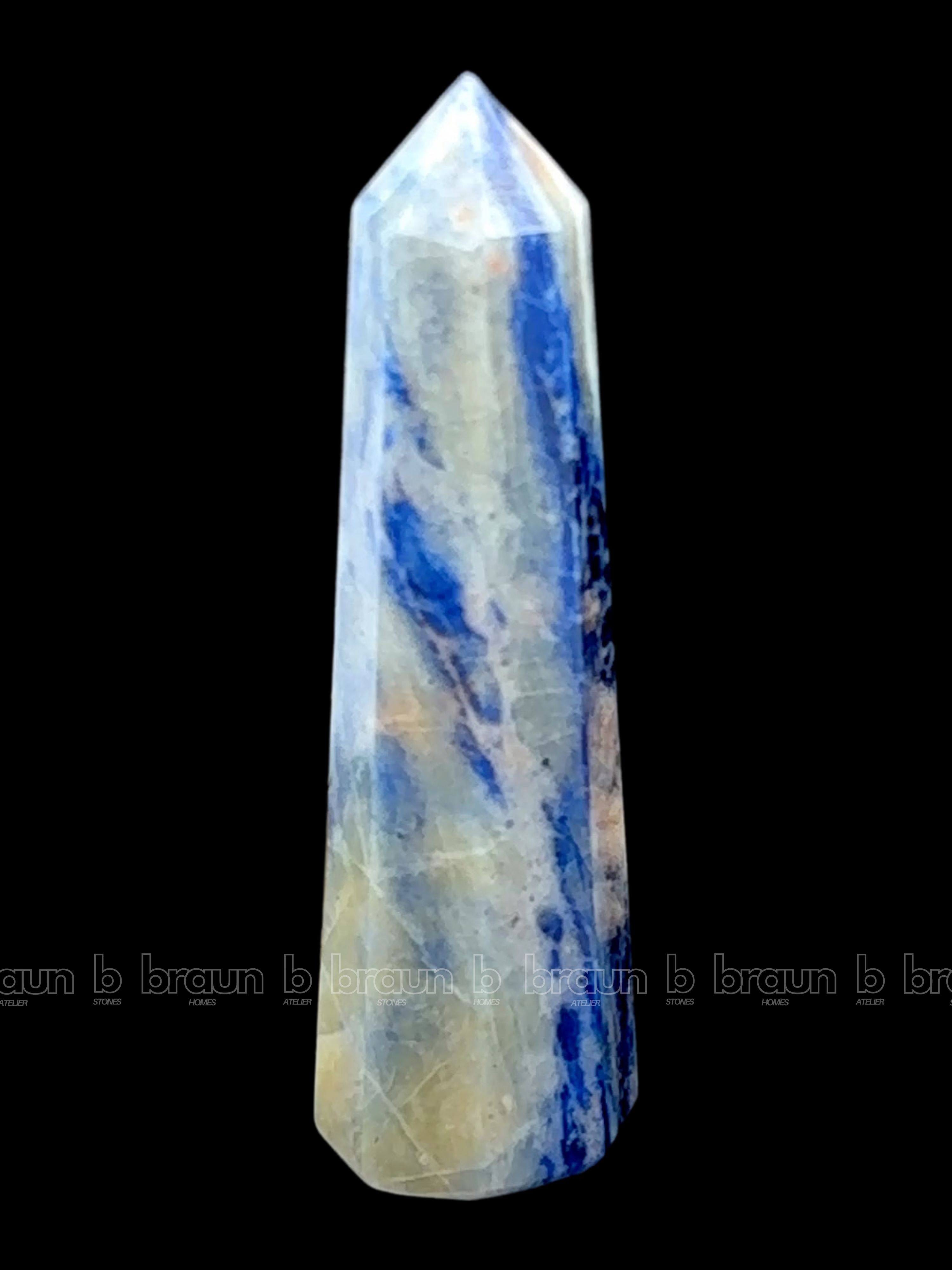 A tall, polished obelisk made of Sodalite, standing upright with smooth, transparent facets that catch and reflect light