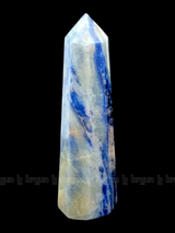 A tall, polished obelisk made of Sodalite, standing upright with smooth, transparent facets that catch and reflect light