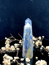 A tall, polished obelisk made of Sodalite, standing upright with smooth, transparent facets that catch and reflect light