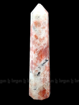 A tall, polished obelisk made of Sunstone, standing upright with smooth, transparent facets that catch and reflect light