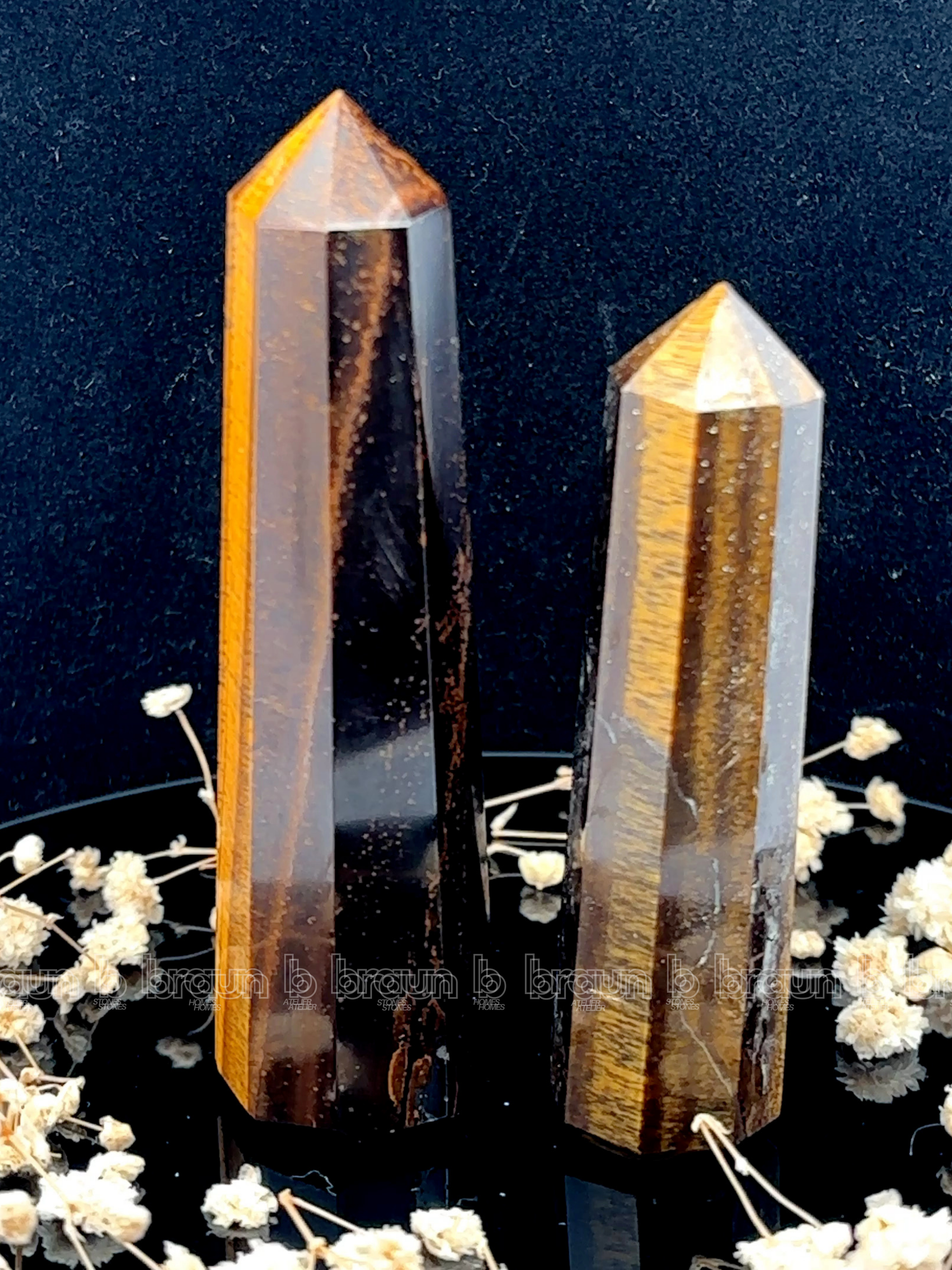 A tall, polished obelisk made of Tiger eye, standing upright with smooth, transparent facets that catch and reflect light