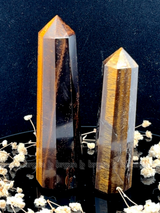 A tall, polished obelisk made of Tiger eye, standing upright with smooth, transparent facets that catch and reflect light