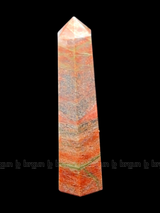 A tall, polished obelisk made of Unakite, standing upright with smooth, transparent facets that catch and reflect light