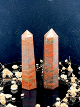 A tall, polished obelisk made of Unakite, standing upright with smooth, transparent facets that catch and reflect light