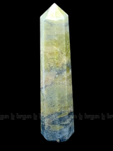 A tall, polished obelisk made of Vasonite, standing upright with smooth, transparent facets that catch and reflect light