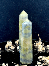 A tall, polished obelisk made of Vasonite, standing upright with smooth, transparent facets that catch and reflect light