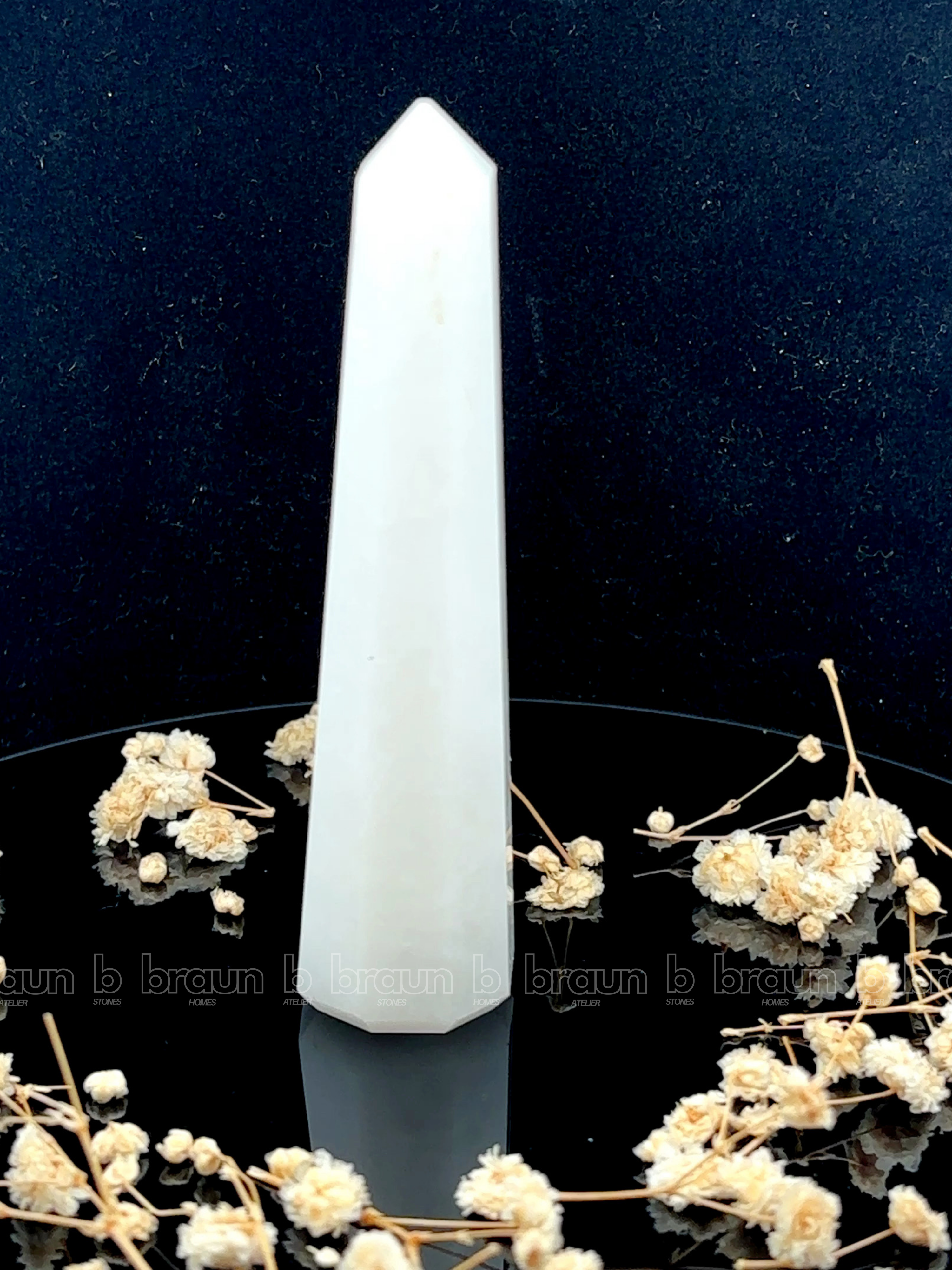 A tall, polished obelisk made of White Quartz, standing upright with smooth, transparent facets that catch and reflect light