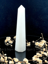 A tall, polished obelisk made of White Quartz, standing upright with smooth, transparent facets that catch and reflect light