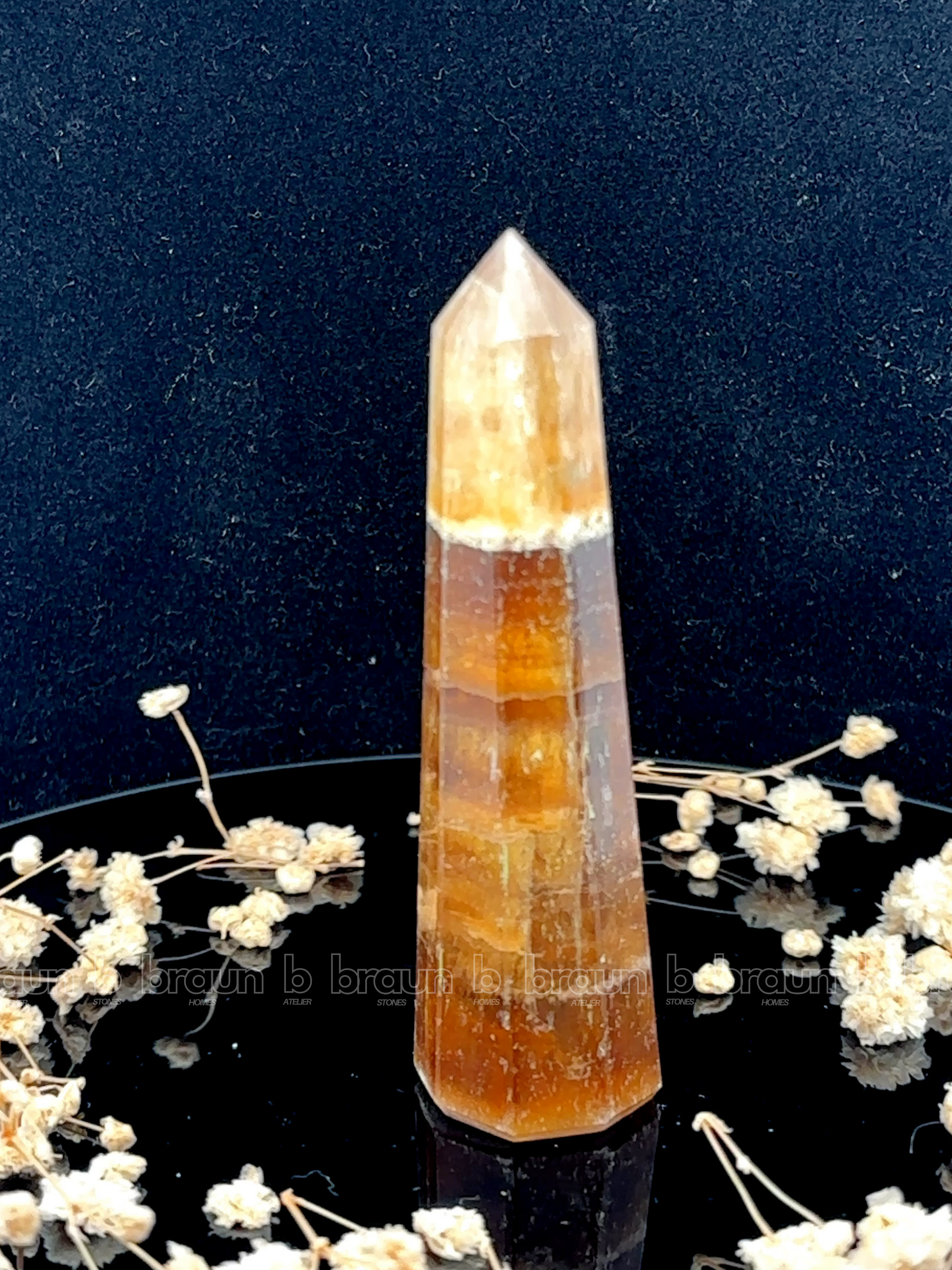 A tall, polished obelisk made of Yellow Fluorite, standing upright with smooth, transparent facets that catch and reflect light